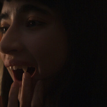 Una chica vampira mira sus colmillos frente al espejo y los toca. Imagen de la película Vampira humanista busca suicida.