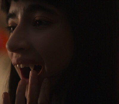 Una chica vampira mira sus colmillos frente al espejo y los toca. Imagen de la película Vampira humanista busca suicida.